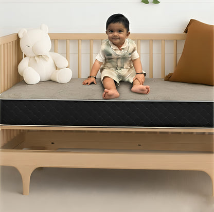 Toddler sitting on a crib mattress in a wooden cot – SleepWell baby and kids mattress